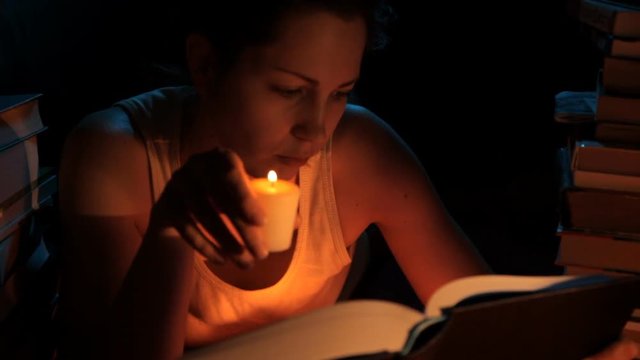 девушка ночью читает книгу со свечей