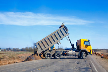 tipper unloads sand on the road. truck dumps sand on the side of the road during roadworks © EvgeniiAnd