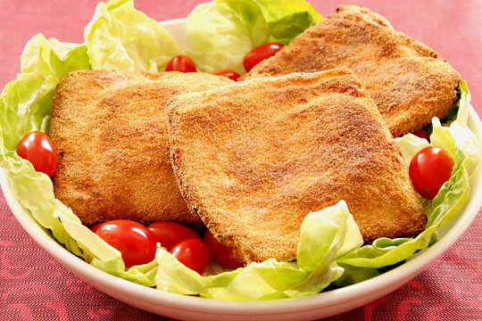 A dish with baked mozzarella in carrozza with green salad and tomatoes cherry. Red background.