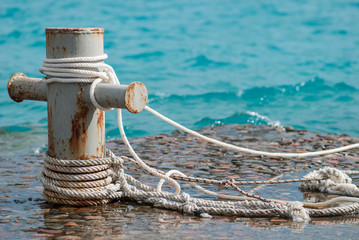 Rusty mooring bollard with ship ropes and  clear turquouse sea ocen water on background