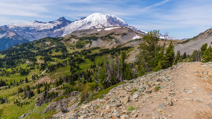 Amazing view at the snowy peaks which rose against the blue of a cloudless sky. Narrow rocky trail high in the mountains.BERKELEY PARK TRAIL, Sunrise Area, Mount Rainier National Park