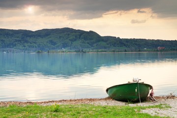 Abandoned fishing paddle boat on bank. Morning Alps lake