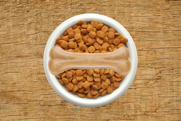 Dry dog food and bone in plate over wooden texture