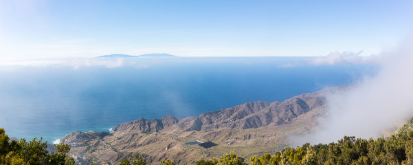 Panorama picture from the overlook Mirador de Alojera to the canyon Barranco del Mono with the village Alojera. Trade winds with scattered clouds comes from the north into the valley.