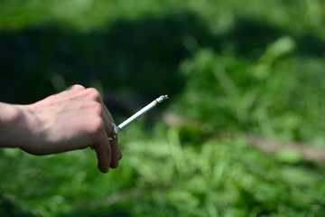 Cigarette in the hand of a woman on the green grass background c