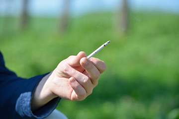 Hand of a man holding a cigarette in hand outside, on a backgrou