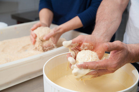 The making of sicilian arancini: sicilian cook diving a rice arancino into beaten eggs and flour