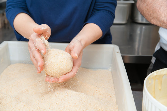 The making of sicilian arancini: sicilian cook covering rice arancini with bread crumbs before frying them