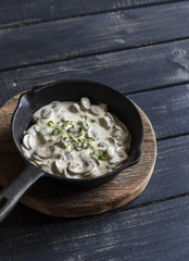 Creamy mushroom sauce in a pan on a wooden rustic board on a dark background