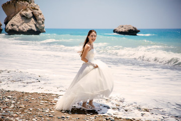 Fototapeta na wymiar outdoor portrait of young beautiful woman bride in wedding dress on beach. Petra tou Romiou - Aphrodite's Rock.