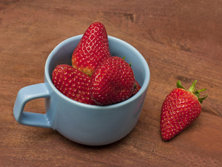 Fresh strawberries in teal blue cup on wooden background texture