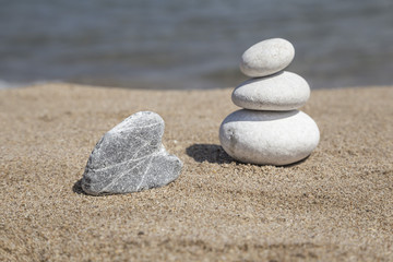 Fototapeta na wymiar heart shaped stone and stack of pebbles on balance on sand