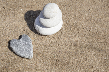 Fototapeta na wymiar heart shaped stone and stack of pebbles on balance on sand