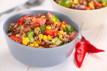 Chili con carne salad made of mincemeat, kidney beans, green bell pepper, tomato, sweet corn and red onions served in bowls with chili on the side (Selective Focus, Focus in the middle of the salad)