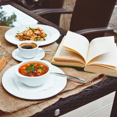 Business lunch with soup, salad and coffee served at the table in the restaurant. On the cloth lay the glasses and the book