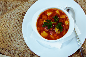 Beautiful red soup with sausage in a white plate with spoon and saucer. Restaurant supply