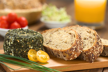 Goat cheese covered with herbs, chives, yellow cherry tomato and slices of wholegrain bread on...