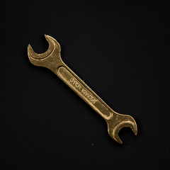 Golden wrench isolated on black background. Symbolic repair tool