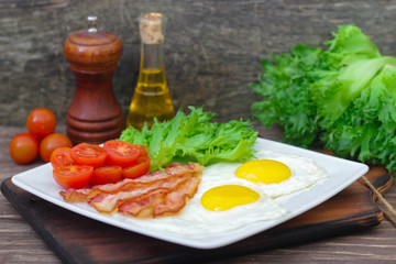 American Breakfast fried Eggs and bacon with tomato and lettuce on a wooden background 