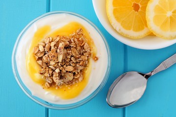 Bowl of lemon flavored Greek yogurt with granola, overhead scene on blue wooden background