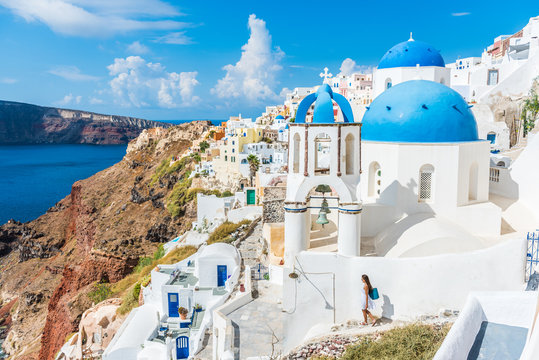Europe, Greek Islands, Greece, Santorini travel tourist vacation destination: City of Oia. Woman on holidays walking on stairs visiting the famous white village by mediterranean sea and blue domes.