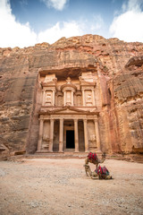 Front view of the famous Al-Khazneh (aka Treasury) with camels resting next to it in the ancient city of Petra (Jordan) - obrazy, fototapety, plakaty
