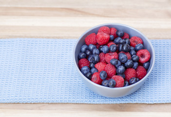 Dessert fresh berries in the bowl. Raspberries and blue-berries on a wooden table. Dessert, fresh berries close-up. 