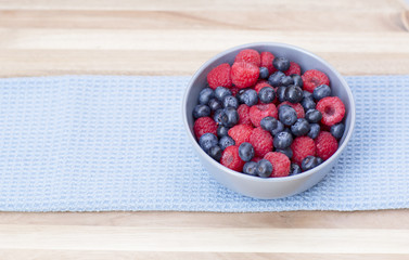 Dessert fresh berries in the bowl. Raspberries and blue-berries on a wooden table. Dessert, fresh berries close-up. 