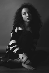 Black and white photo of beautiful sad young business woman sitting on wooden floor. looking at...
