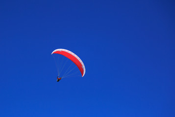 Paraglider with red parapent in a clear, blue sky.