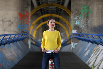 Beautiful Asian woman in blue jeans and yellow sweater standing on a bridge