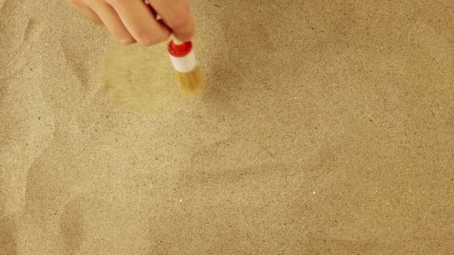 Discovering book under warm desert sand, archeologist hand with brush sweeping the sandy dust.