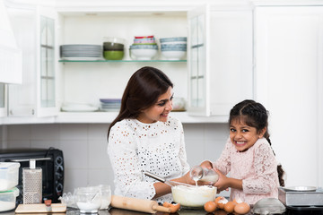 Cute Indian girl pouring milk into bowl with flour