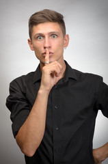 man asking to keep quiet finger near mouth, isolated on grey wall background