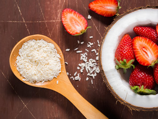 Half coconut with strawberries and shredded coconut on dark brown rustic wooden background. Closeup