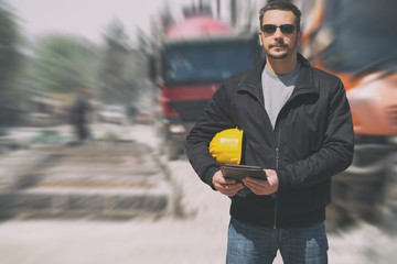 Construction engineer posing with blurred trucks and machines in the background.