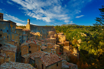 Sorano - tuff city in Tuscany. Italy. View to the clock tower and roofs of the town with green trees and blue sky.