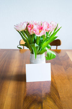 Tulips in blue vase and blank card on wooden dining table. Selective focus.