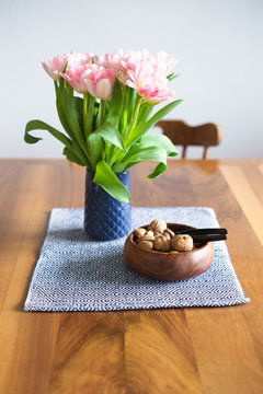 Tulips in blue vase and nuts in wooden bowl on wooden dining table. Selective focus on the nuts.