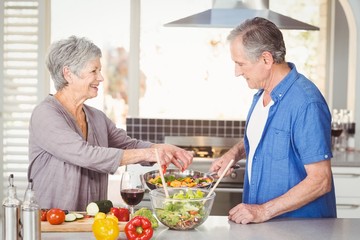 Side view of happy senior couple preparing food while standing at kitchen counter