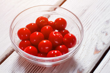 Tomatoes in a glass bowl. Bowl with small ripe tomatoes. Vegetables on white wooden table.  Ingredient for a salad.