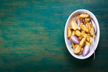 Oven-baked cut potato with red onion and Italian herbs, rustic, vintage or country style in a round bowl on an old vintage green wooden background, top view, with free space for text