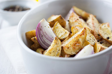 Oven-baked cut potato with red onion and Italian herbs, rustic, vintage or country style in a round...