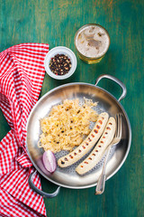 White grilled sausages with sauerkraut or cabbage, black pepper and fresh cold beer in a vintage pan on an old vintage green wooden background, top view