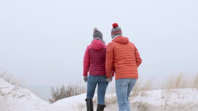 Couple climbing a sand dune and running down a beach in winter white time. Follow shot, gimbal stabilized camera movement. 
