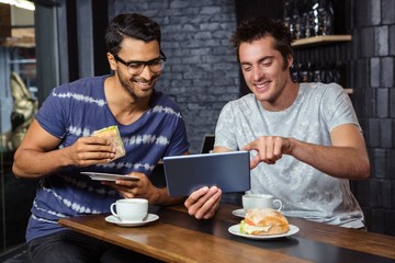 Fototapeta na wymiar Friends using a tablet while eating sandwiches