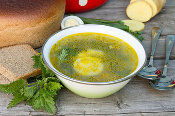 Green nettle soup in a bowl, spoons, bread against a wooden board