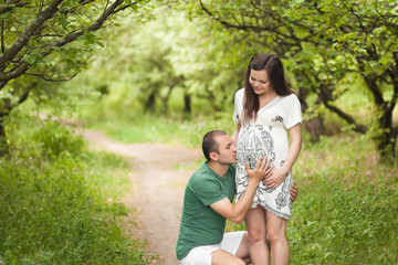 Fototapeta premium Happy couple waiting for baby. Future father kisses and hugs pregnant belly. Future mother is smiling and looking on man an her belly. New family concept. Paternity.