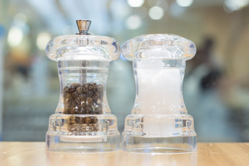 Salt and pepper inside clear container on wooden table with blur