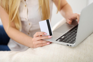 Happy woman doing online shopping at home . Close- up of a hand holding a credit card next to a laptop